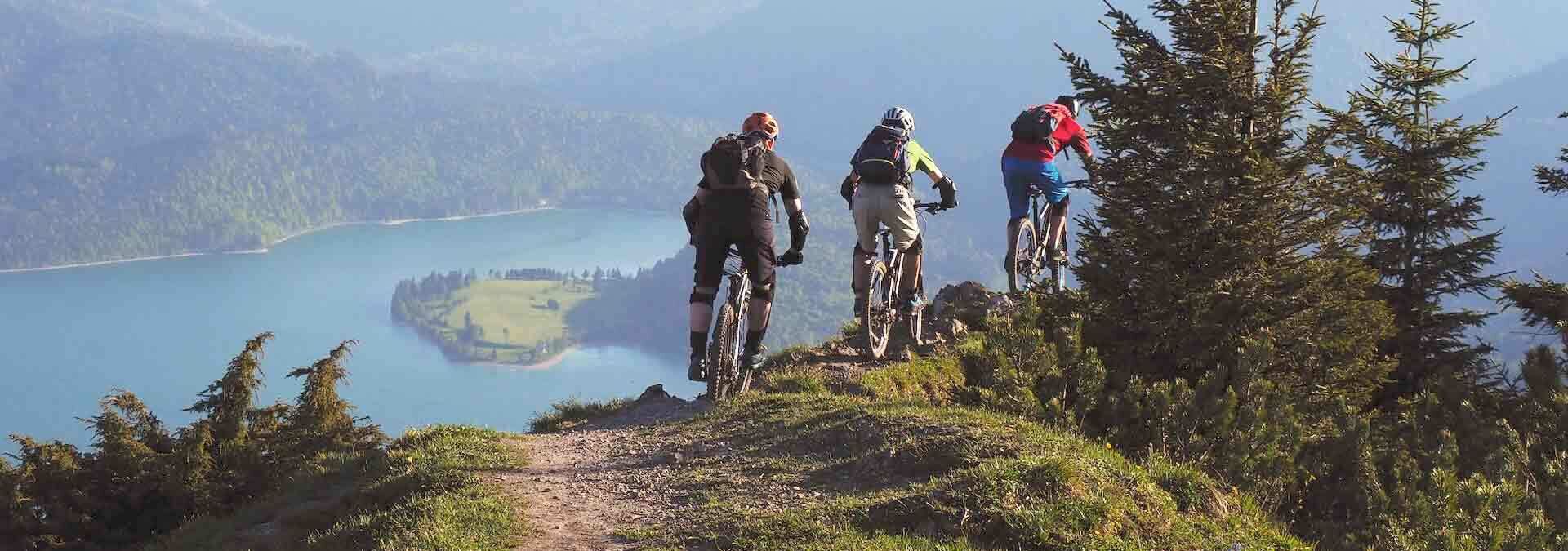 drei-mountainbiker-radeln-auf-dem-gipfel-eines-huegels-im-hintergrund-ist-ein-bergsee drei-mountainbiker-radeln-auf-dem-gipfel-eines-huegels-im-hintergrund-ist-ein-bergsee